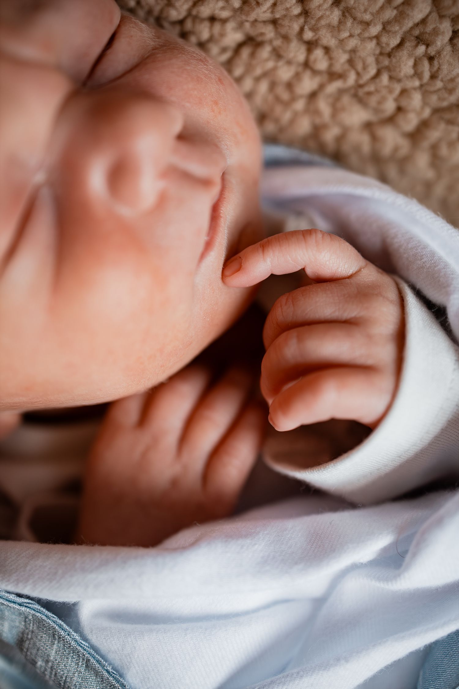 Close-up of tiny newborn baby fingers grasping a soft white blanket.
