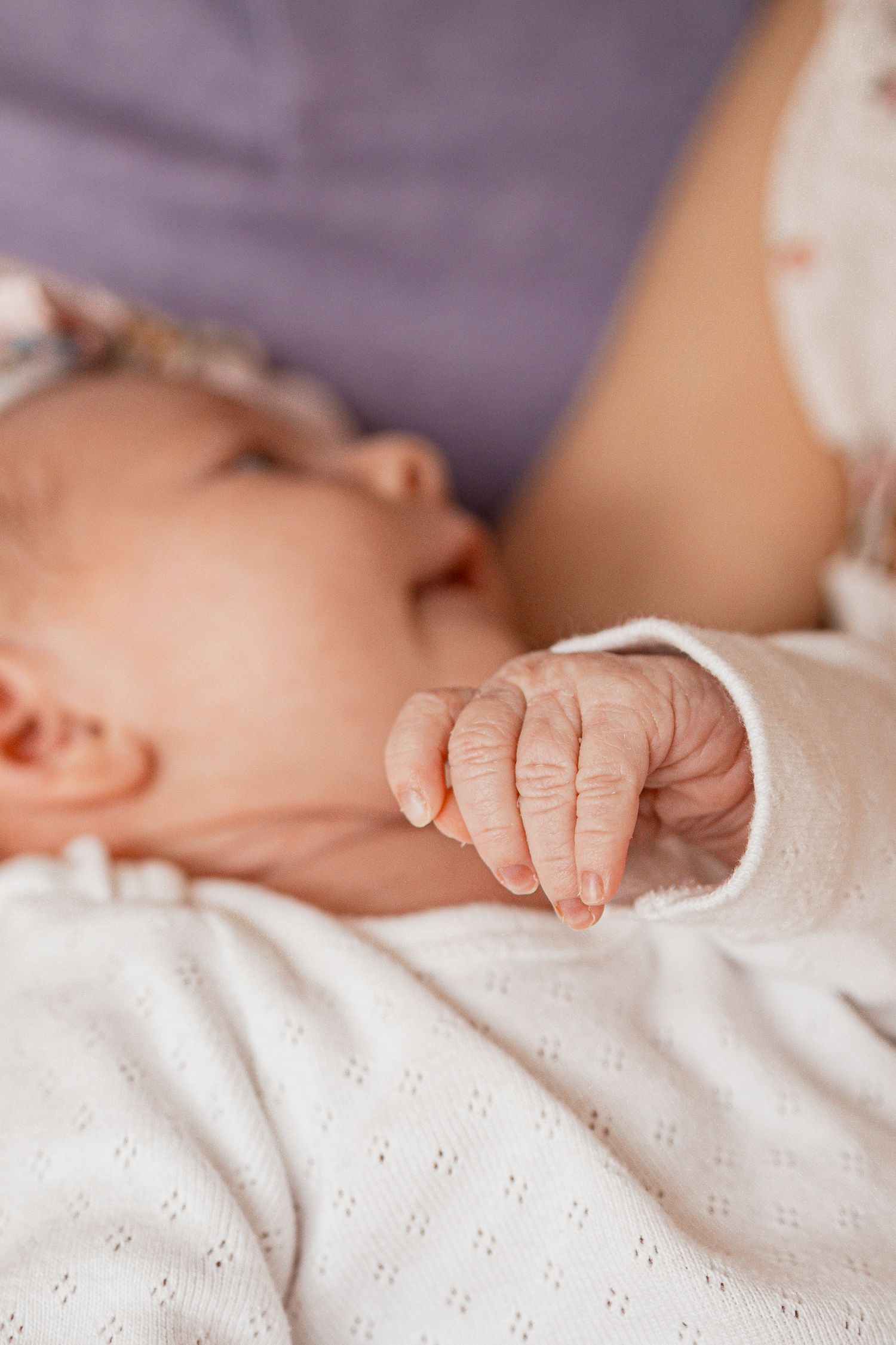 Close-up view of tiny baby fingers grasping white eyelet fabric.