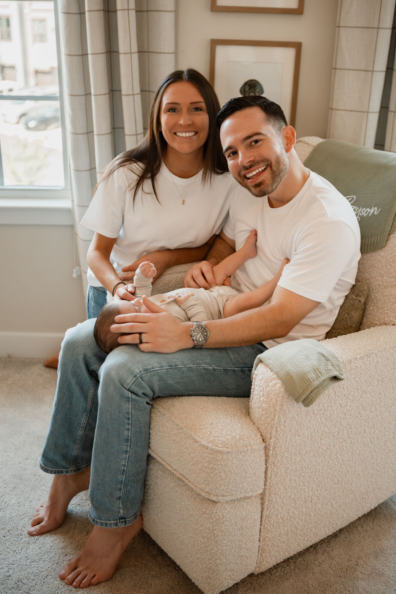 A couple lounges comfortably on a cream-colored armchair in matching white t-shirts and jeans.