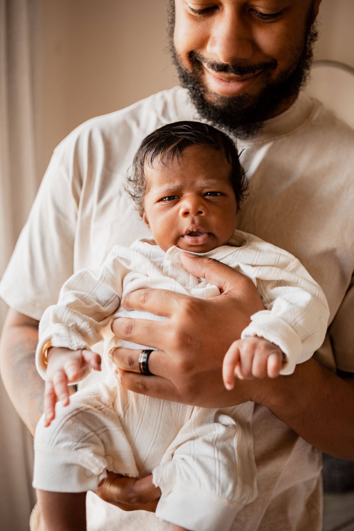 Parent in white shirt tenderly holds newborn baby dressed in light colored clothing.