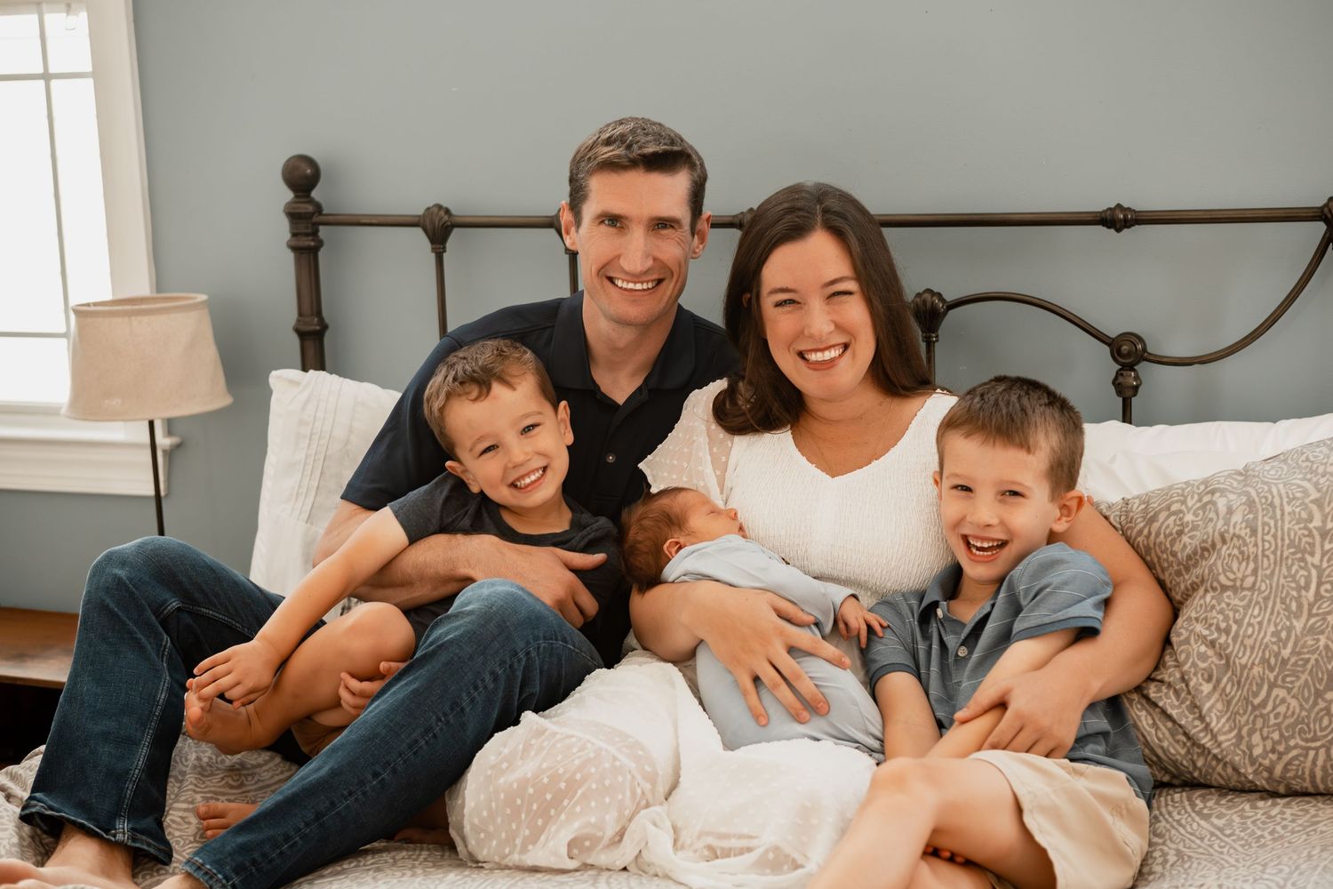 Five family lifestyle photos show candid moments of a family relaxing together on a white bed.