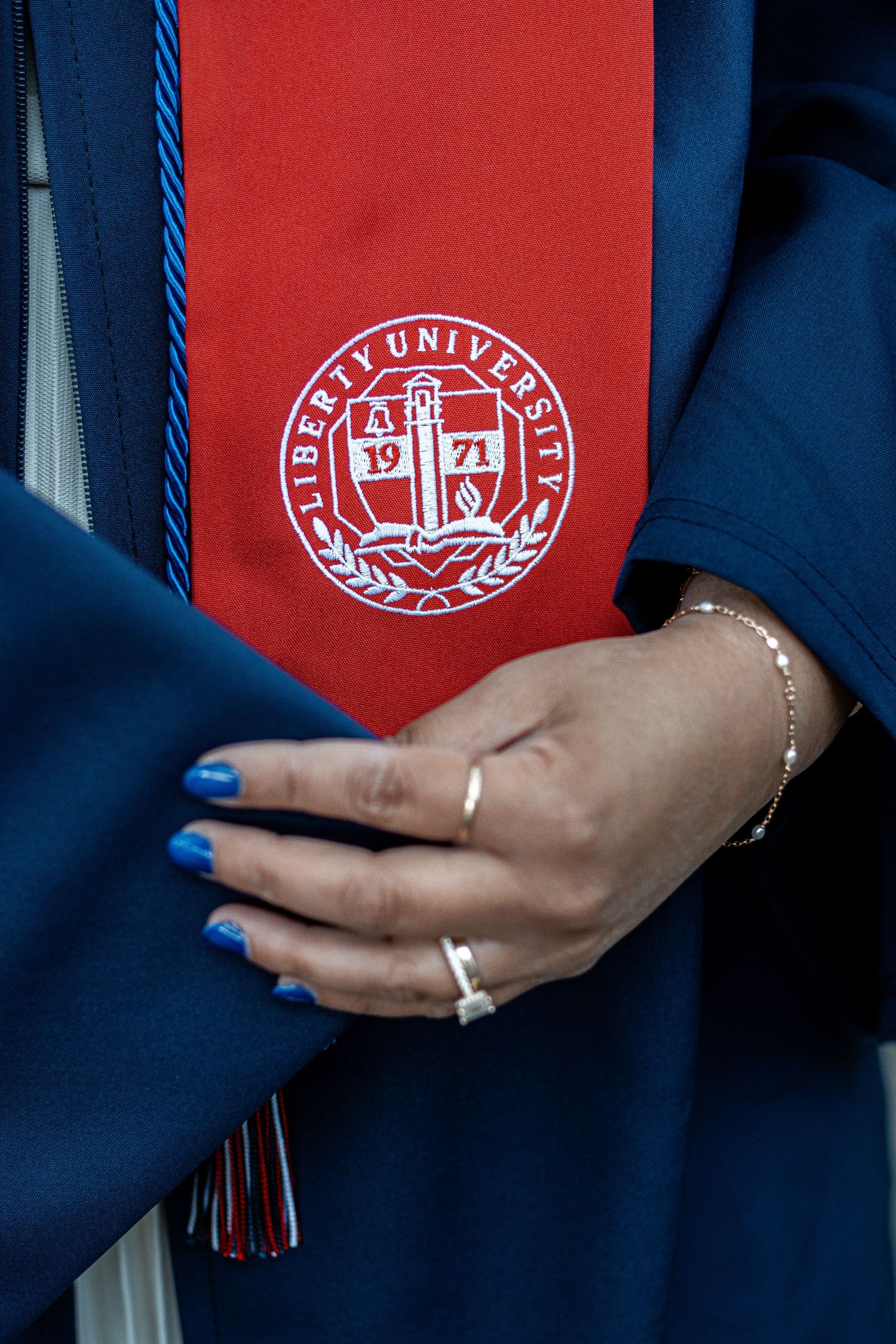 Close up of hands with blue nails and rings against Liberty University graduation stole and emblem.