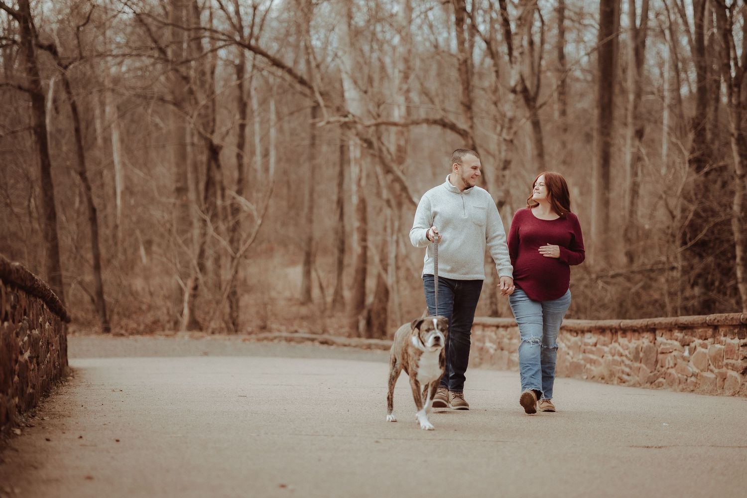 A couple walking their dog on a peaceful autumn path through the woods in warm sepia tones.