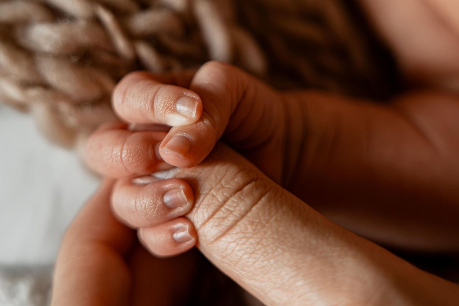 A newborn baby's tiny fingers gently gripping an adult's finger, showcasing the delicate bond between parent and child.