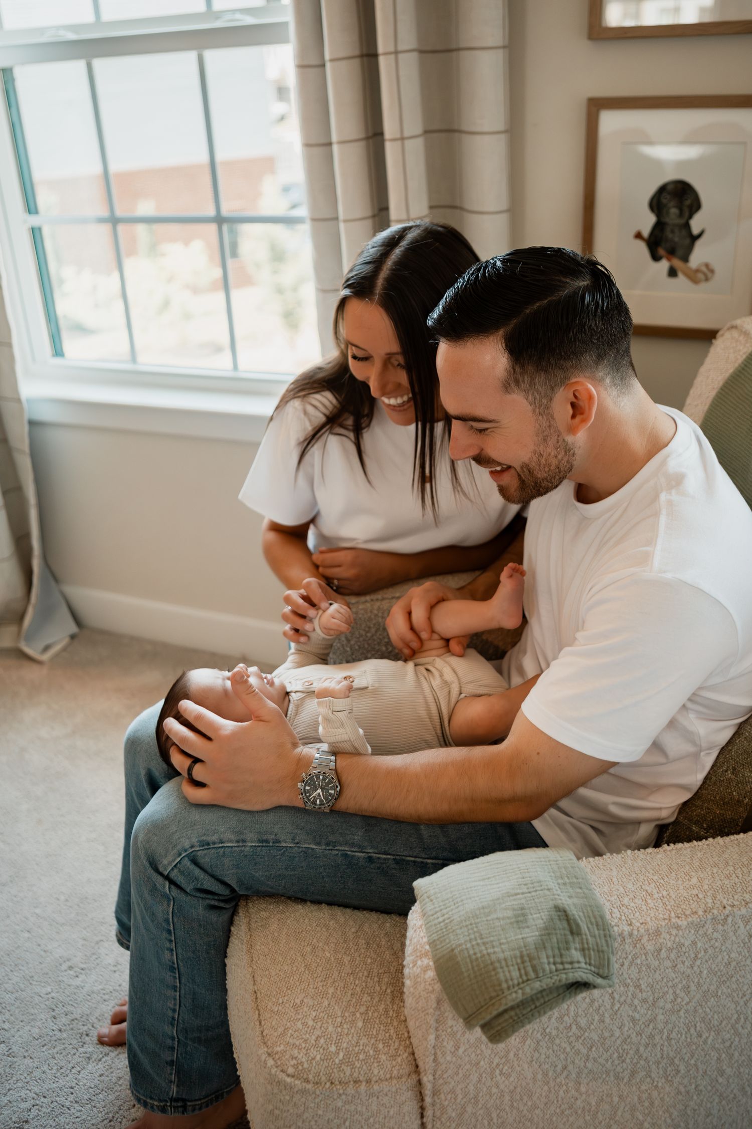 A couple in white shirts sit together on a beige couch in matching outfits while sharing a casual moment.