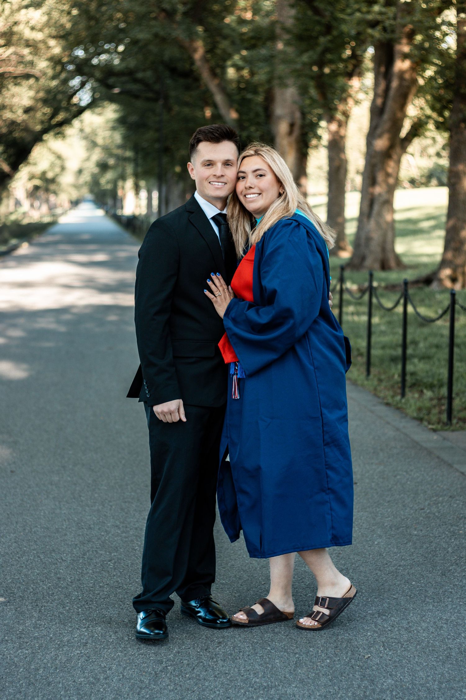 Graduation portraits of a couple in formal attire on a tree-lined campus path.