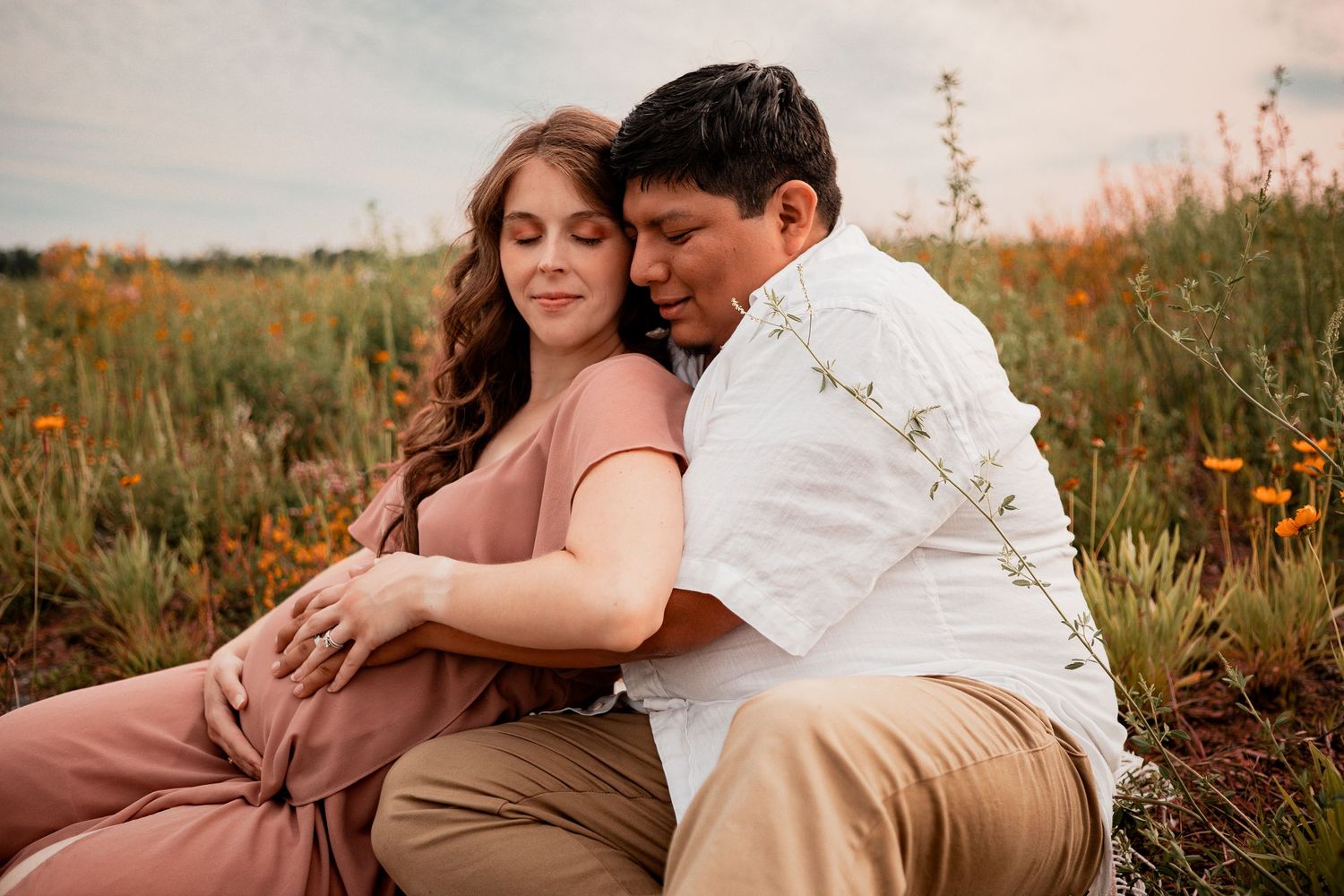 Couple sitting together in dreamy orange wildflower field at sunset.