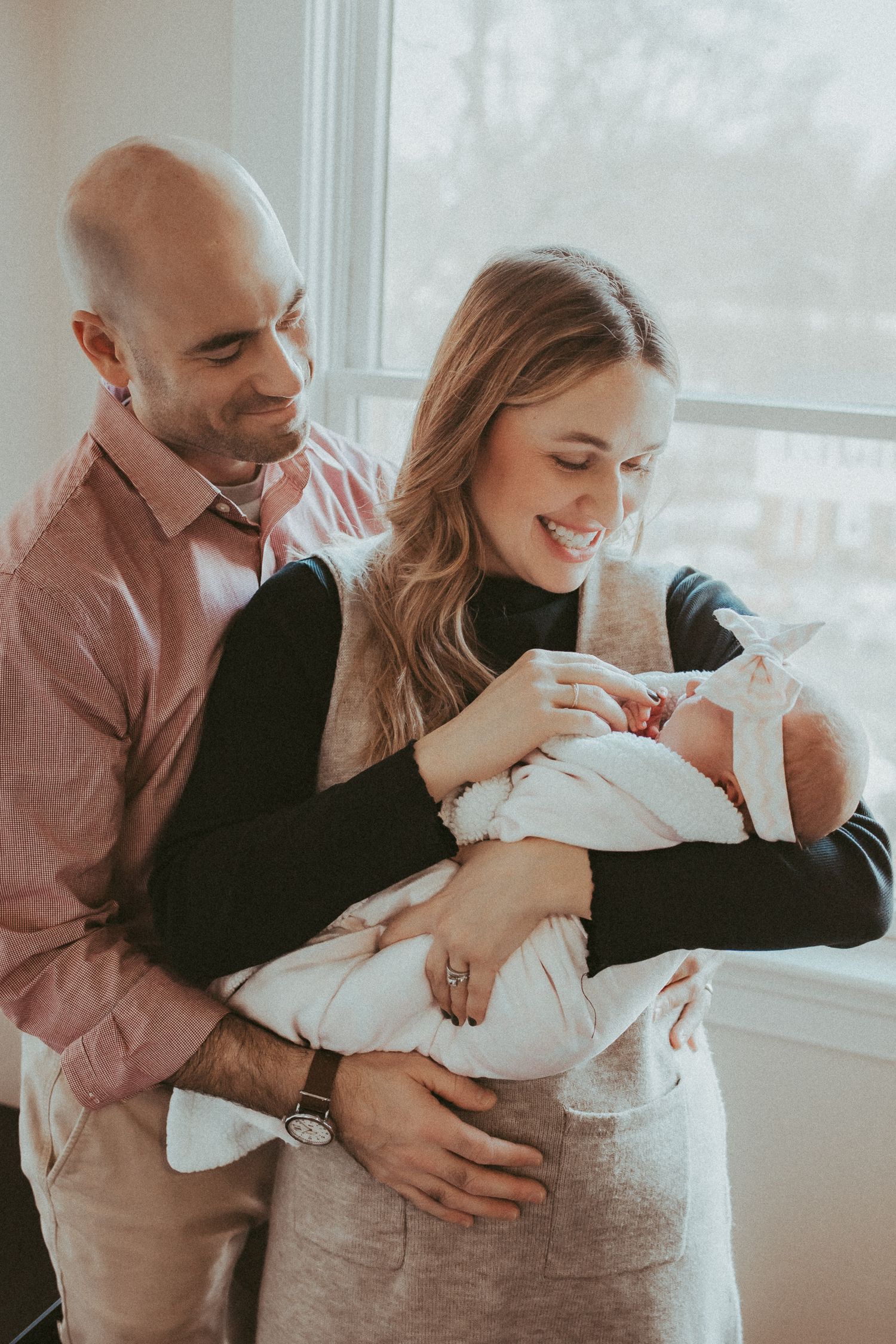 A couple shares joyful moments together while embracing near a bright window in a cozy indoor setting.