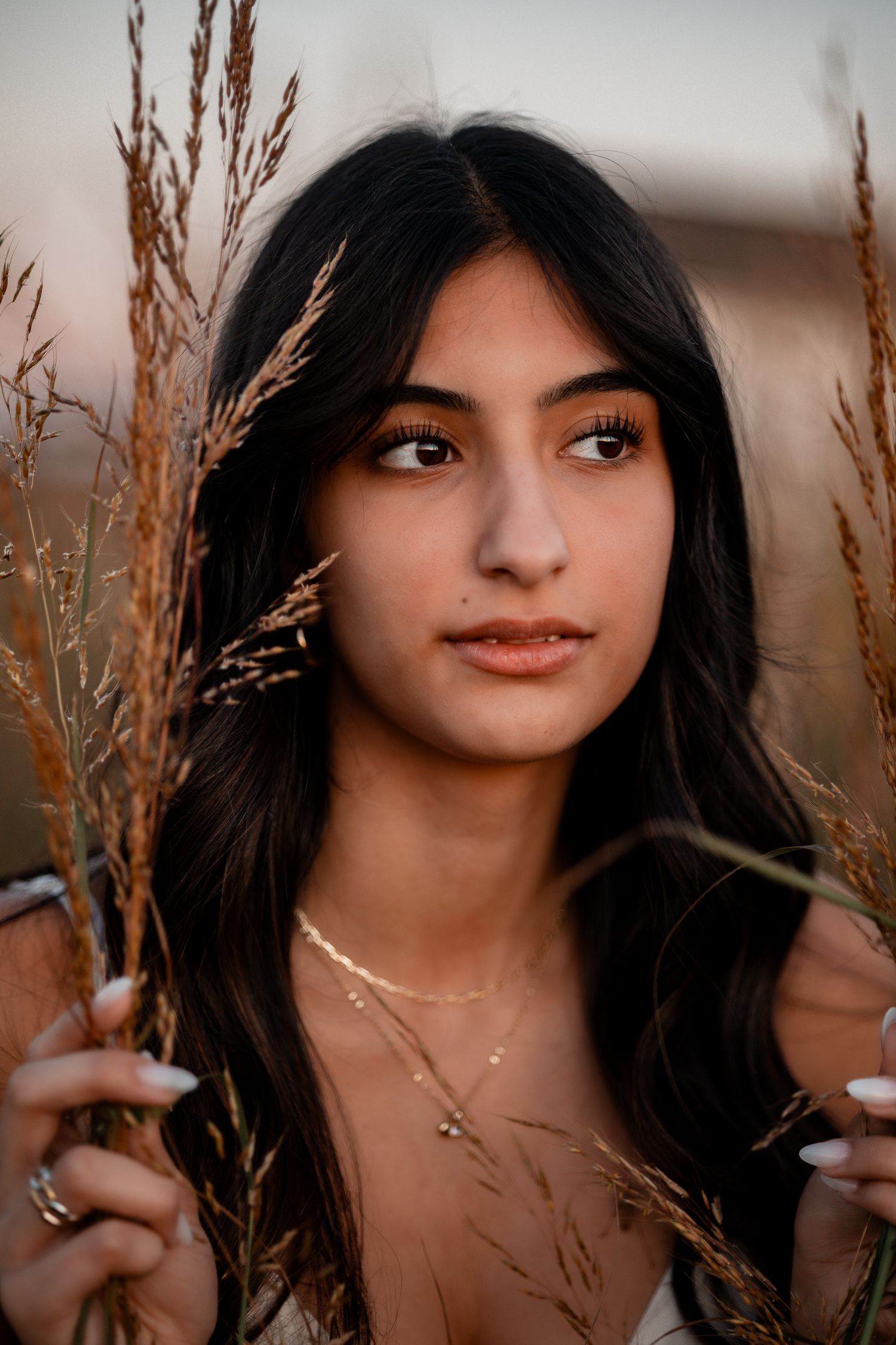 A dreamy golden hour portrait in tall grass, featuring a person in a white dress wearing dainty jewelry.