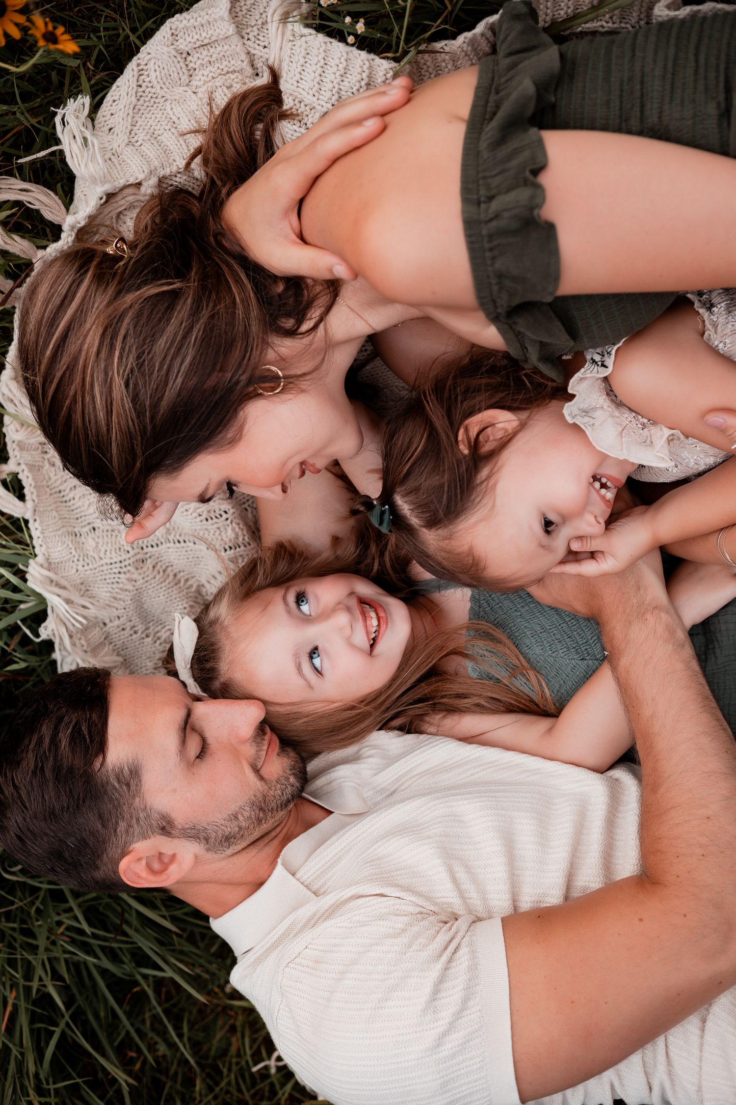 A group lies together on a blanket in the grass, creating an intimate family moment outdoors.