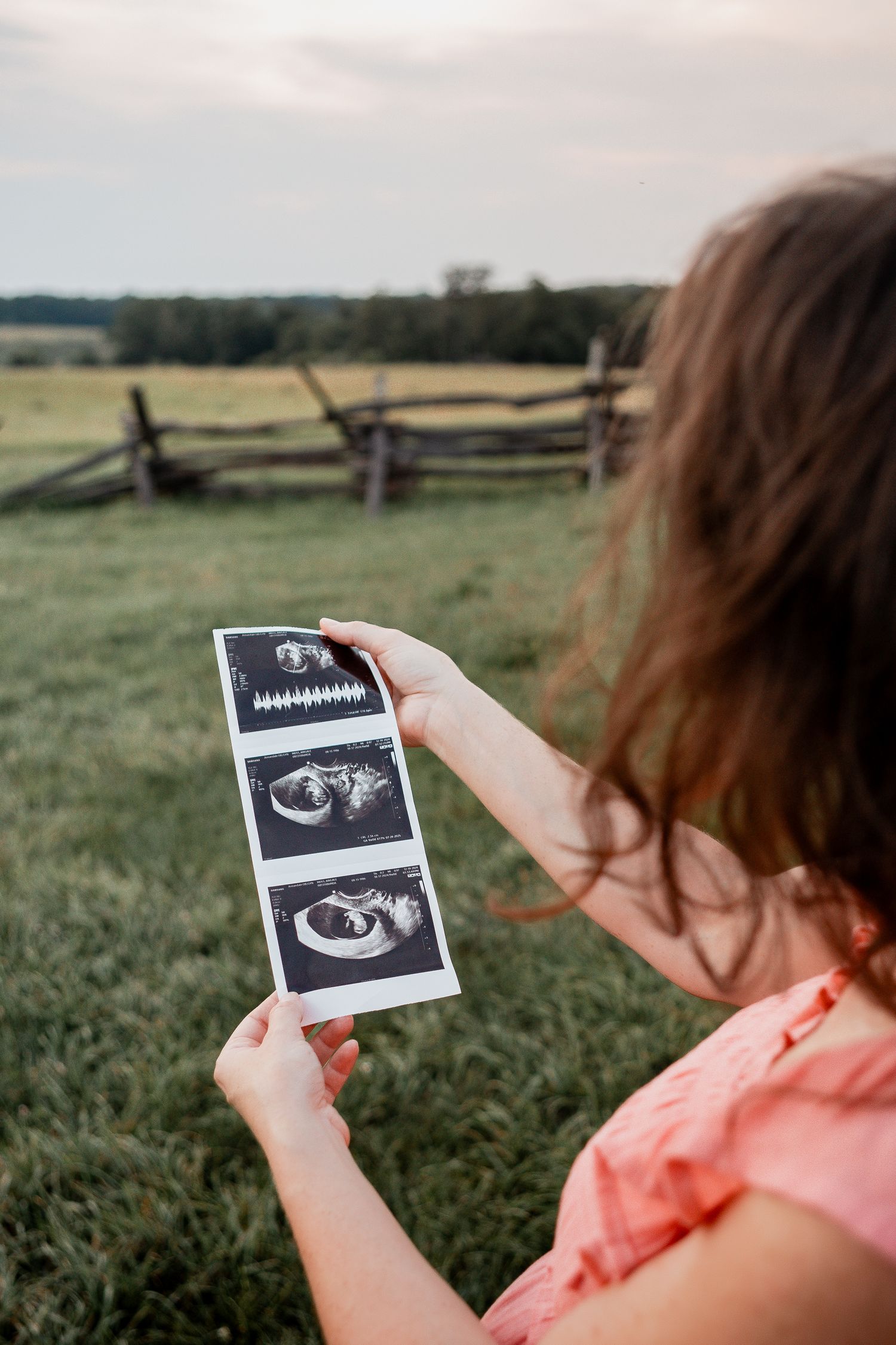 Someone holds up black and white ultrasound photos in a grassy field at sunset.