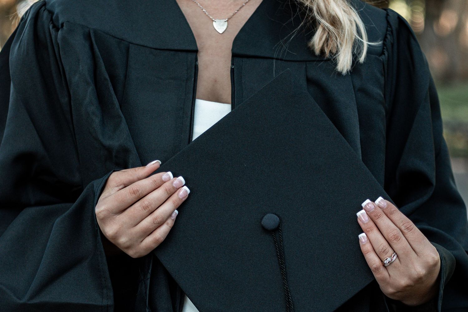 Close-up view of hands with white manicured nails holding a black graduation gown.