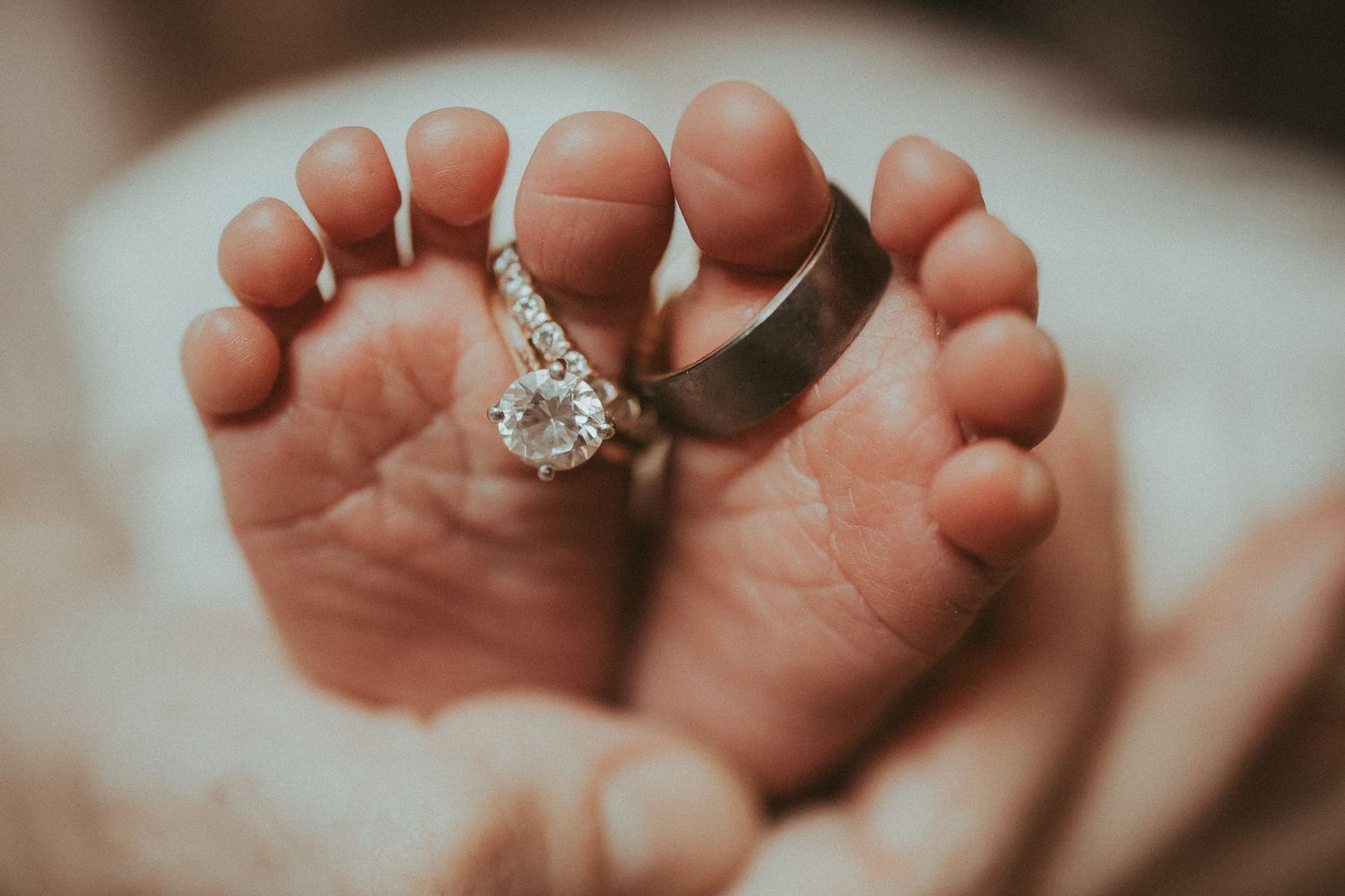 Close-up view of hands gently holding a sparkling diamond engagement ring against a soft blurred background.