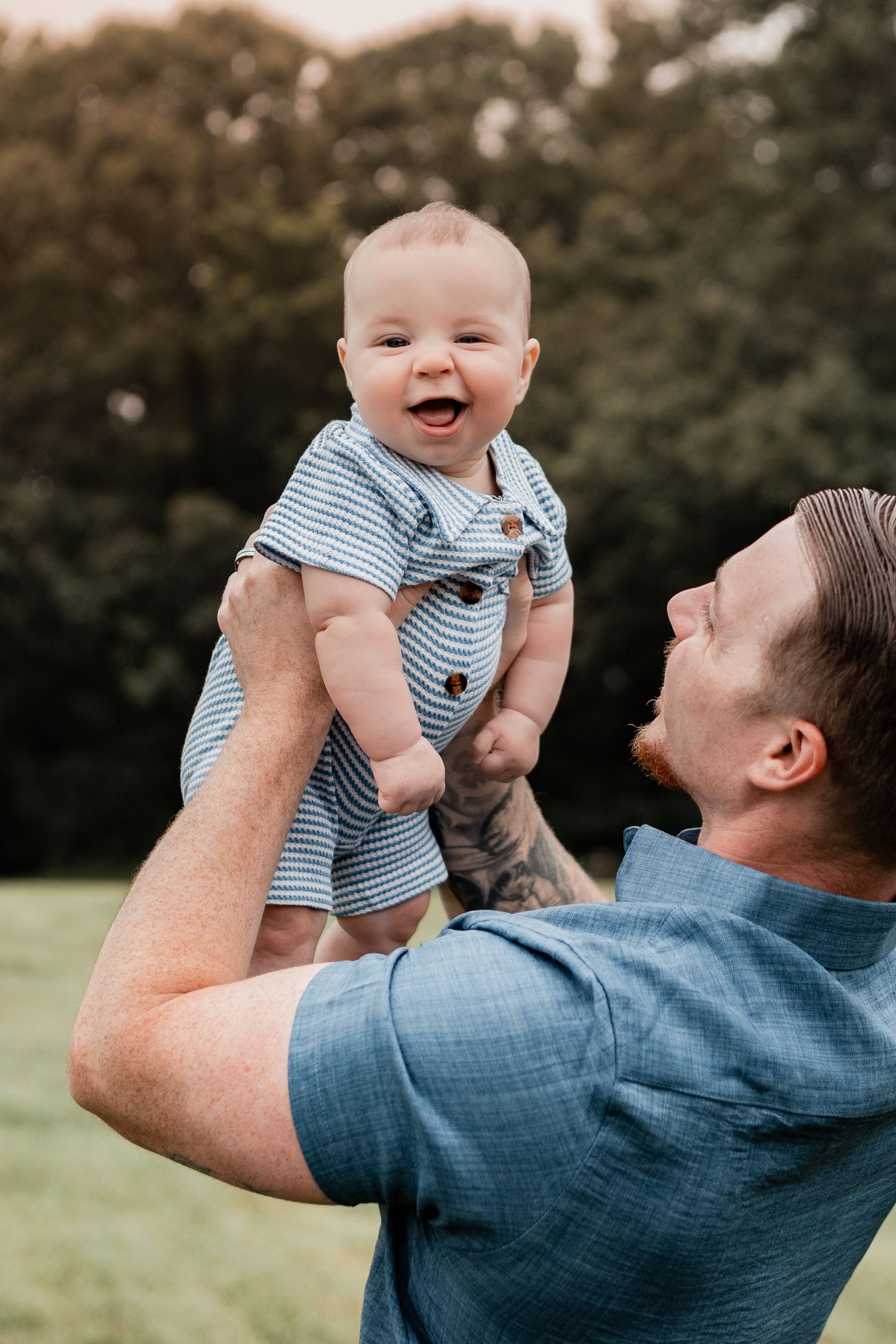 A baby in striped clothing laughs with pure joy while being held up against a sunset backdrop.