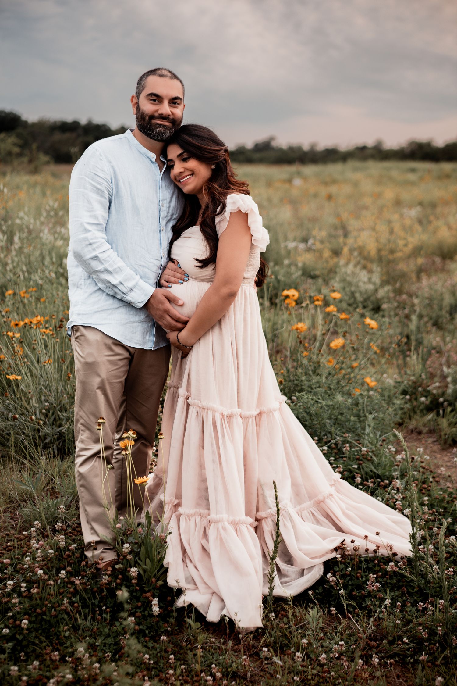 A couple embraces in a blooming wildflower field wearing white and blush pink clothing during a romantic photo session.