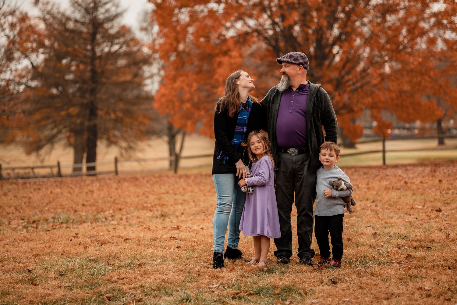 Family enjoying a fall photoshoot together on ground covered with orange autumn leaves.