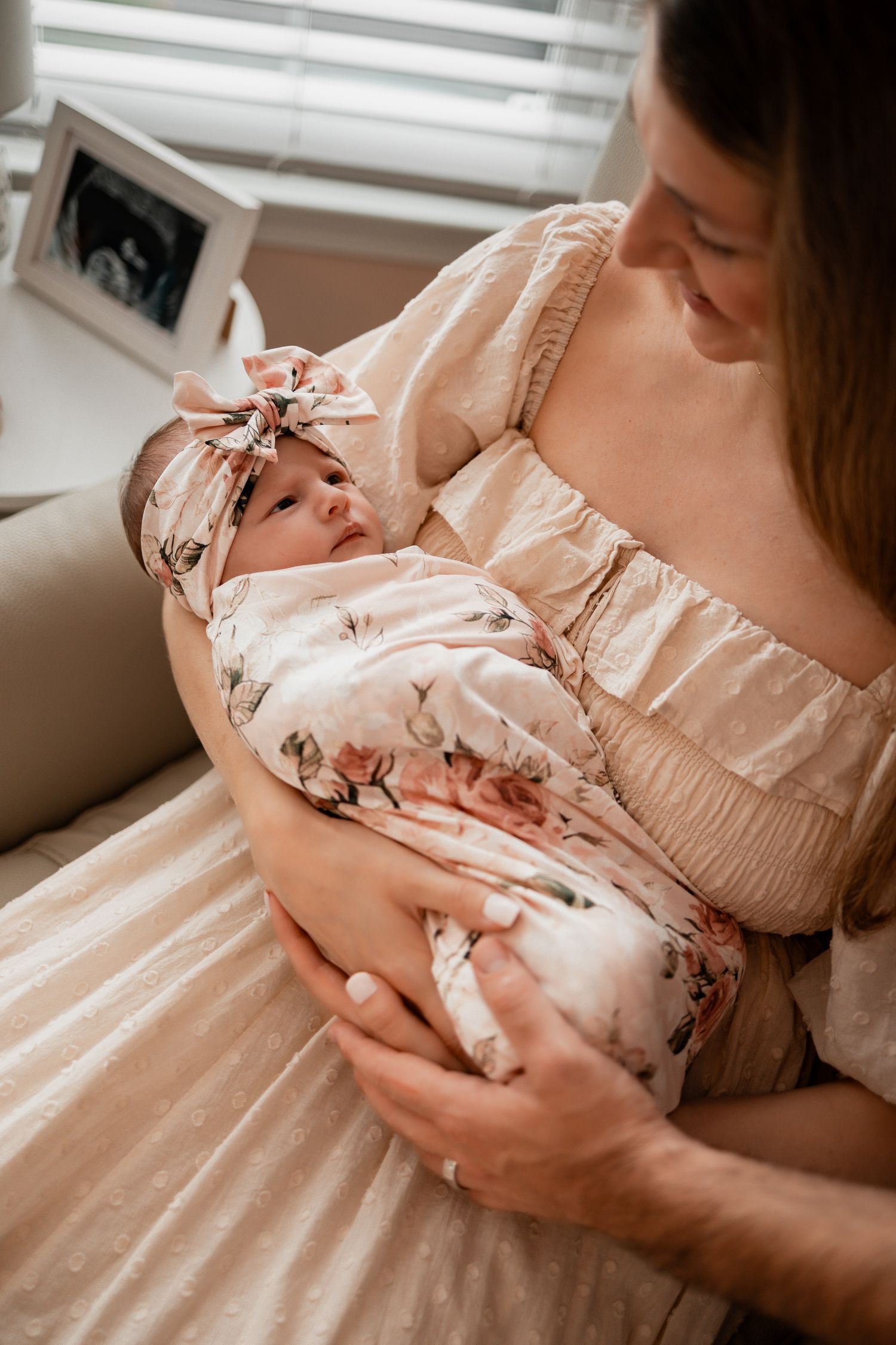 Close-up shots of a sleeping newborn being held in floral-patterned clothing against a cream-colored background.