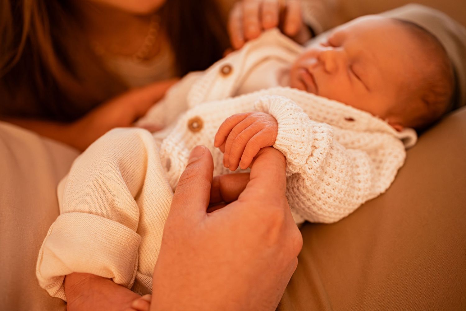 Close-up shot of parents cradling newborn baby in soft natural lighting.