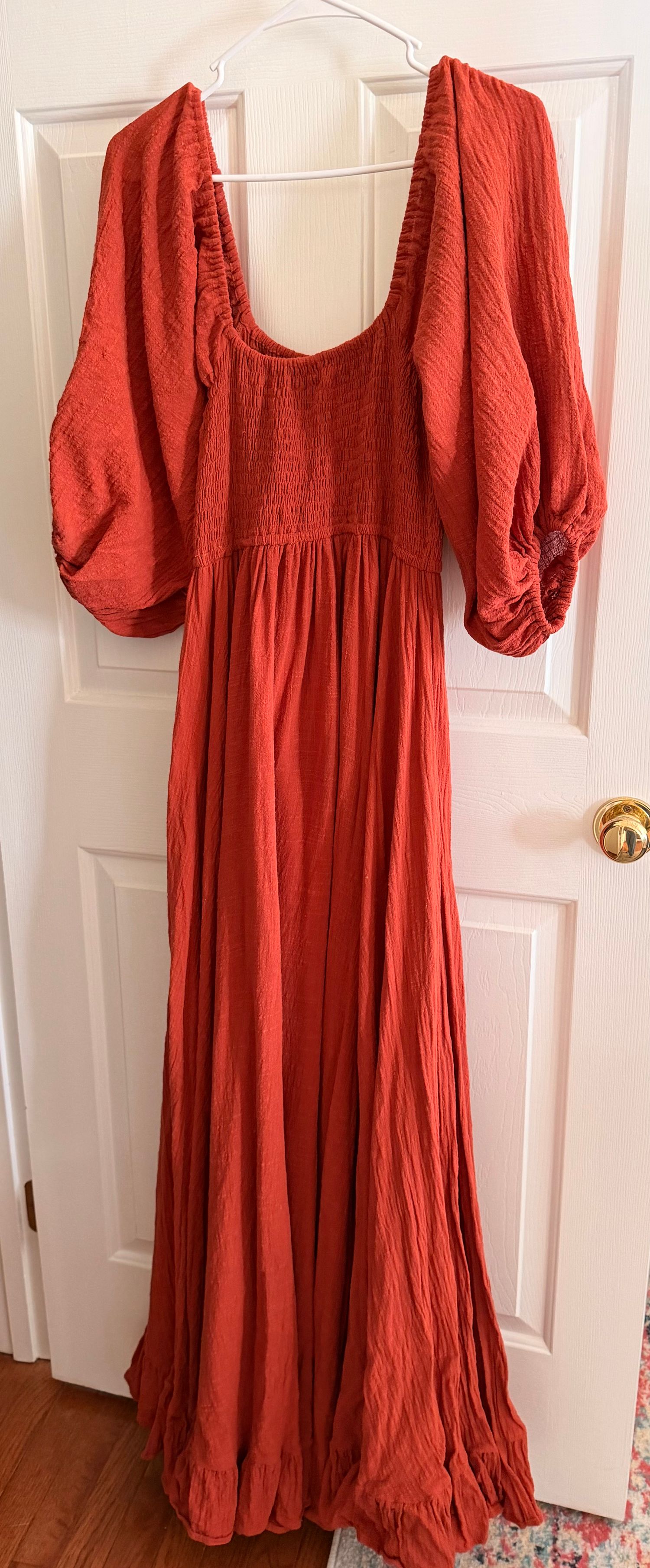 Rust orange maxi dress with balloon sleeves, smocked bodice, and flowing skirt, hanging on a door hanger.