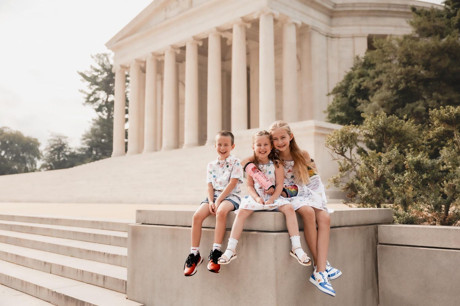 Three children sitting on a stone wall at the Jefferson Memorial in Washington DC on a sunny day.