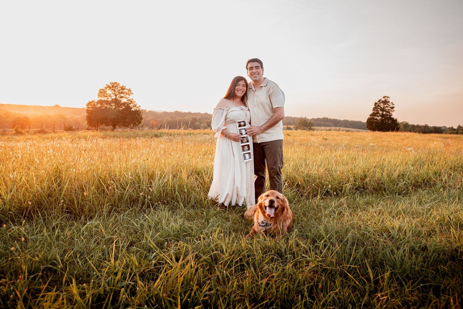 A couple stands together embracing in a golden sunlit field during sunset while wearing white and casual attire.