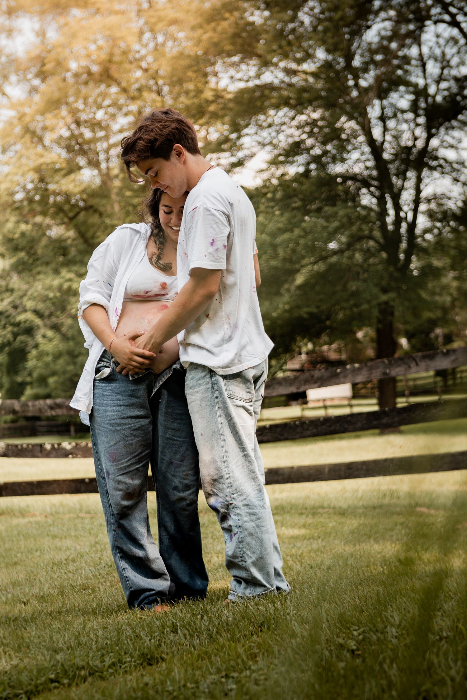 Couple in casual white shirts and jeans sharing intimate moments on grassy lawn during golden hour.