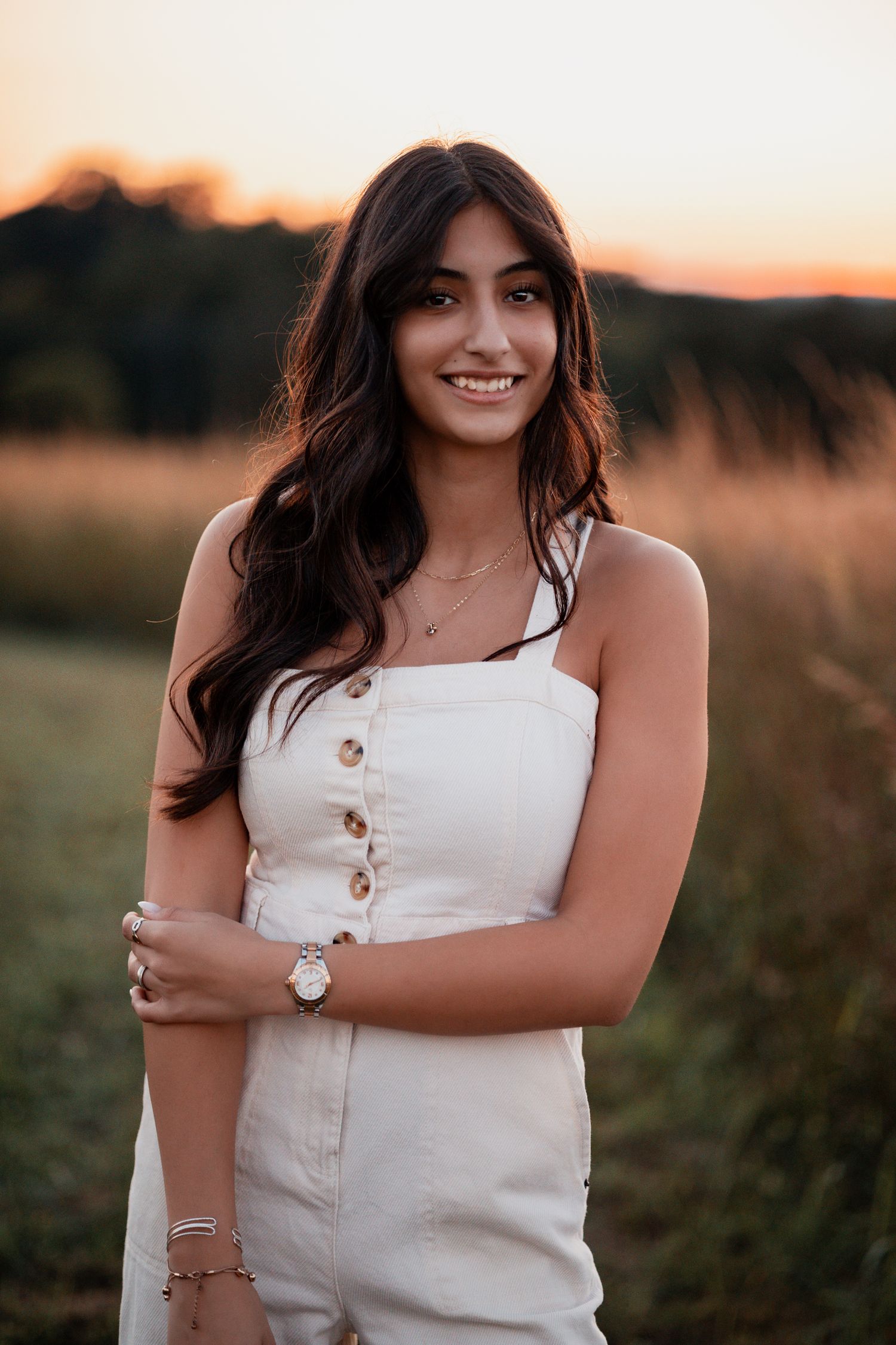 Portrait in a white sleeveless dress with buttons against golden sunset light in a grassy field.