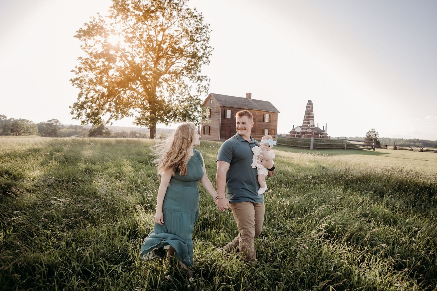 Two figures walk through a grassy field at sunset towards an old church building with a tower in the distance.