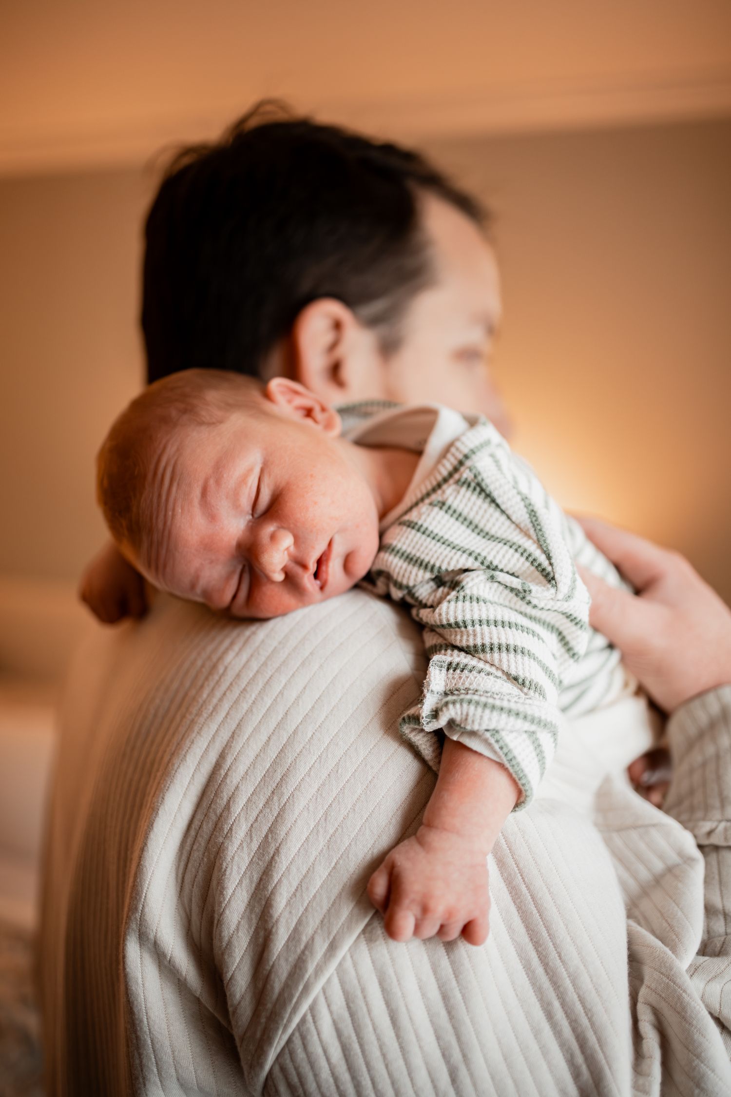 A peaceful newborn baby sleeping on someone's shoulder while wearing a striped outfit.