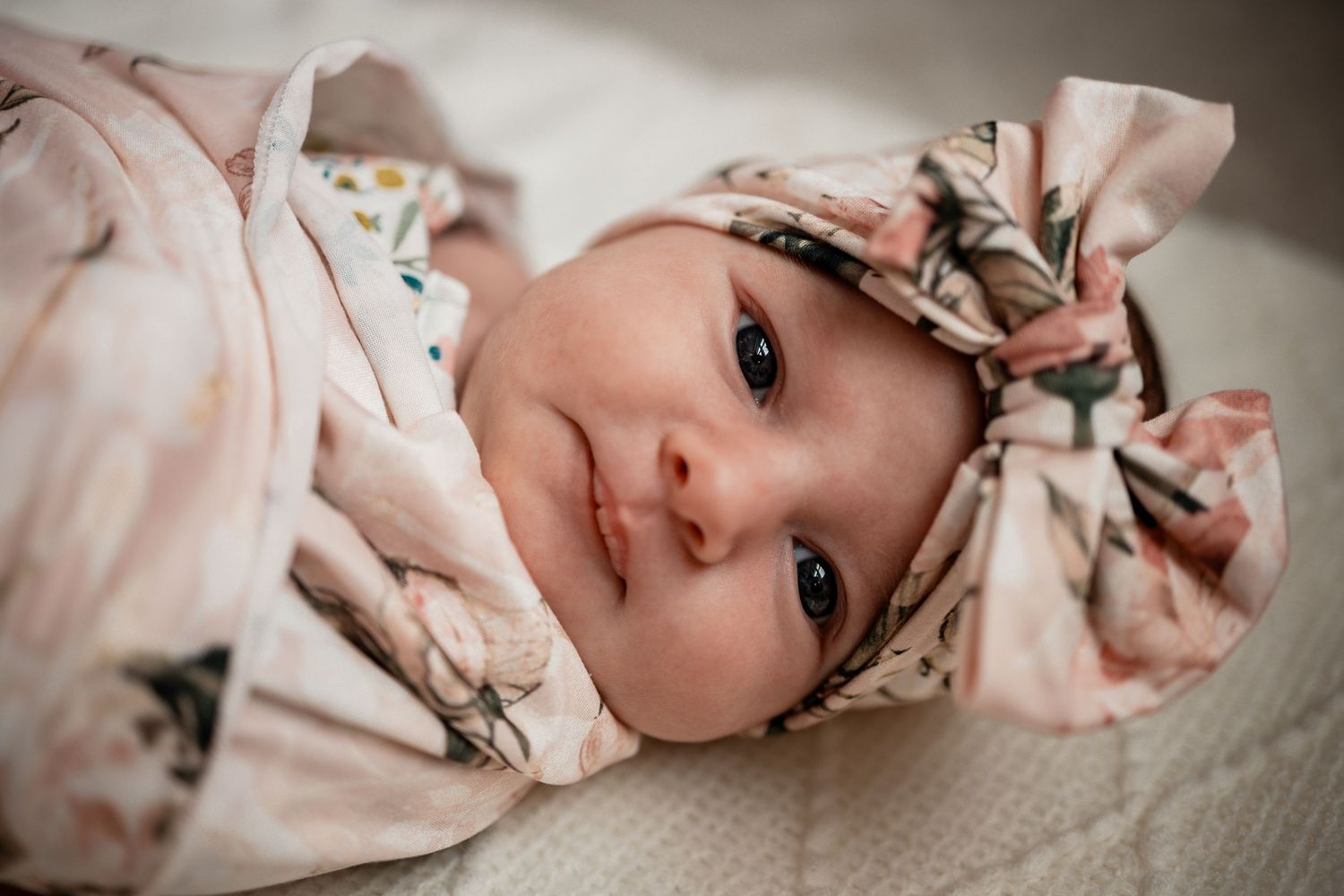 Baby wearing pink floral outfit lies on white blanket in series of connected photos.