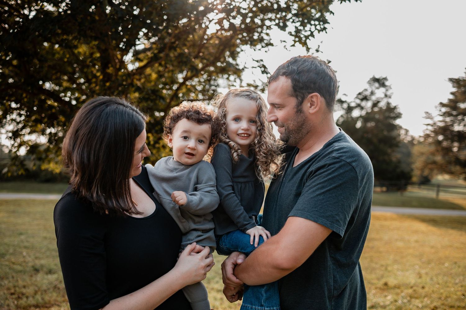 A family shares tender moments together in a grassy field during sunset, creating heartwarming outdoor portraits.