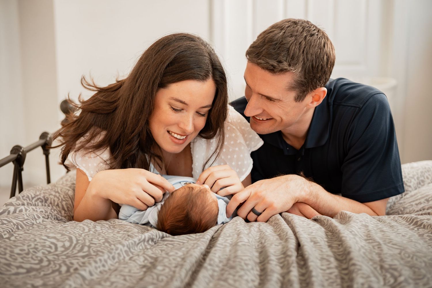 Happy couple lying on a grey couch while interacting with their brown French Bulldog puppy.