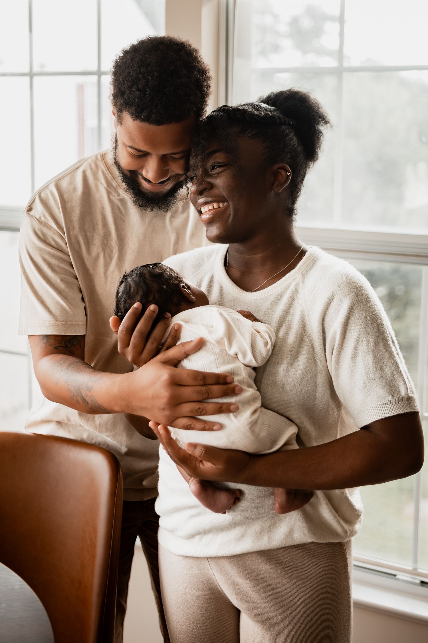 Parent in white t-shirt holding and lovingly gazing at newborn baby in three tender moments by window.