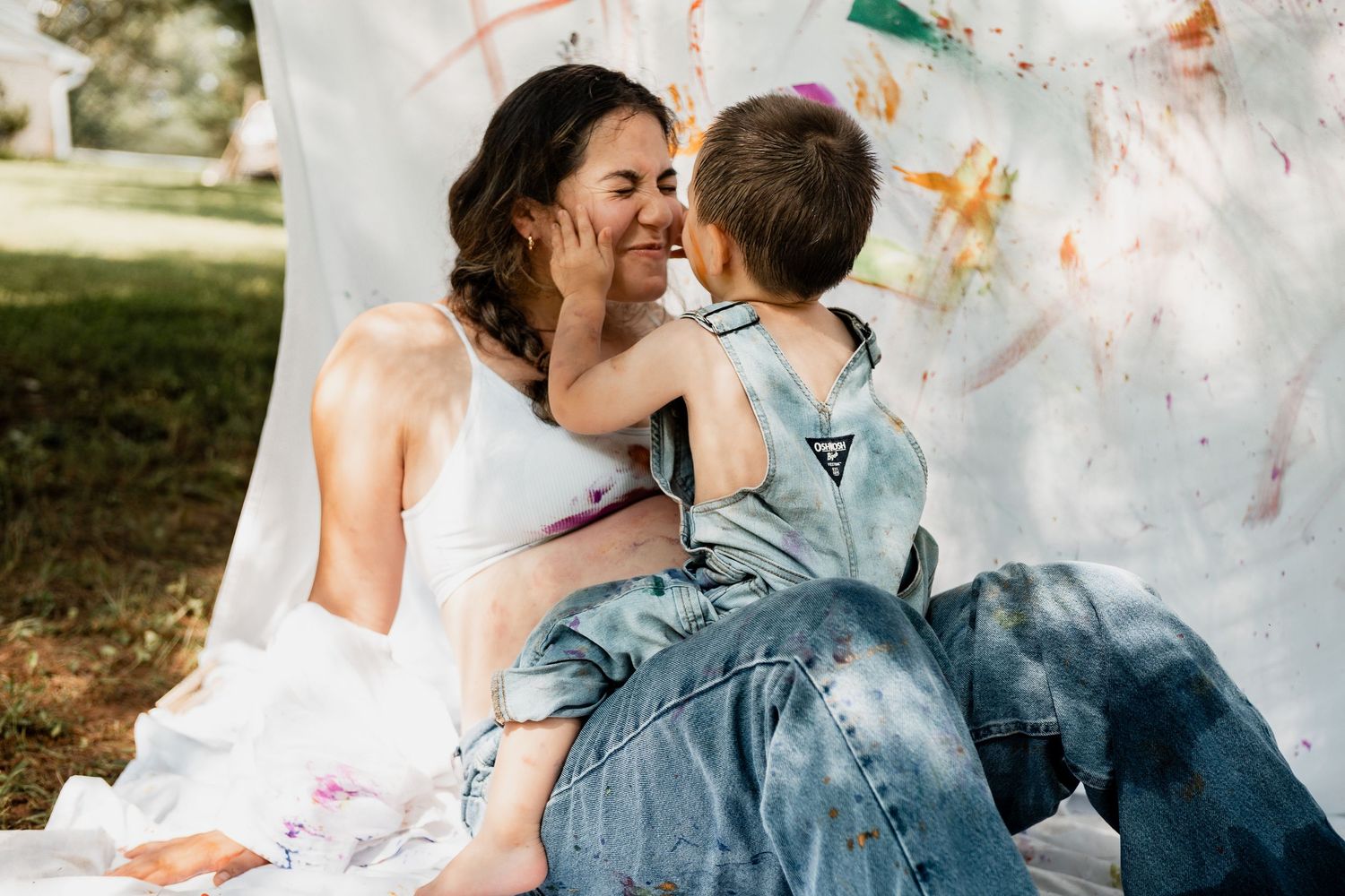 A joyful moment shared during a messy paint session against a white backdrop outdoors.