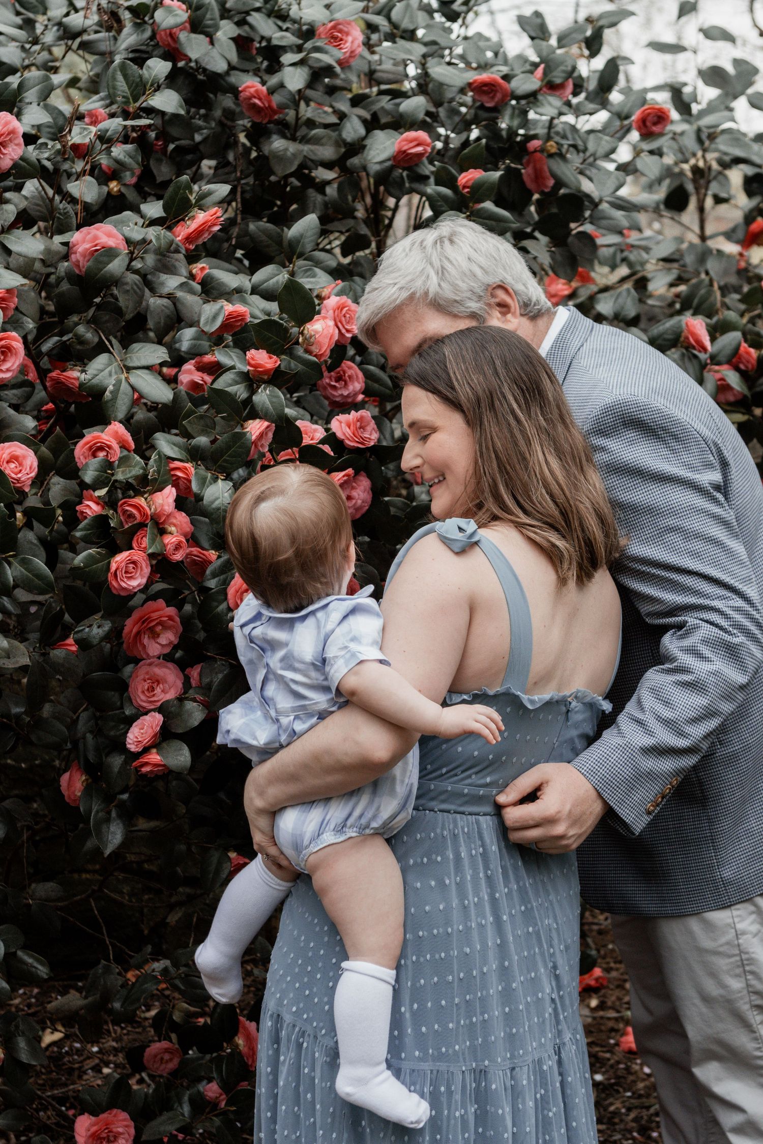 A series of candid family moments against a backdrop of pink roses and green foliage in a garden setting.