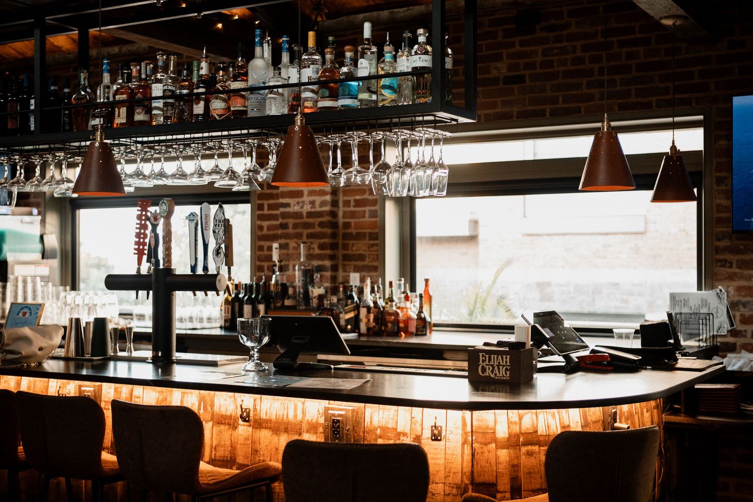 Bar interior with exposed brick walls, copper pendant lights, and wine glass storage.