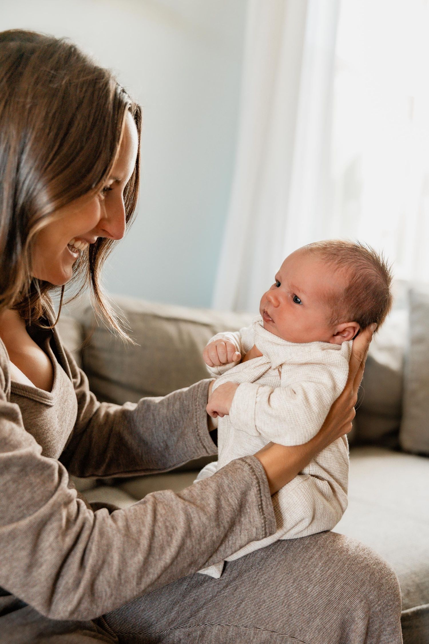 Smiling mother holding and gazing at her alert newborn baby indoors.