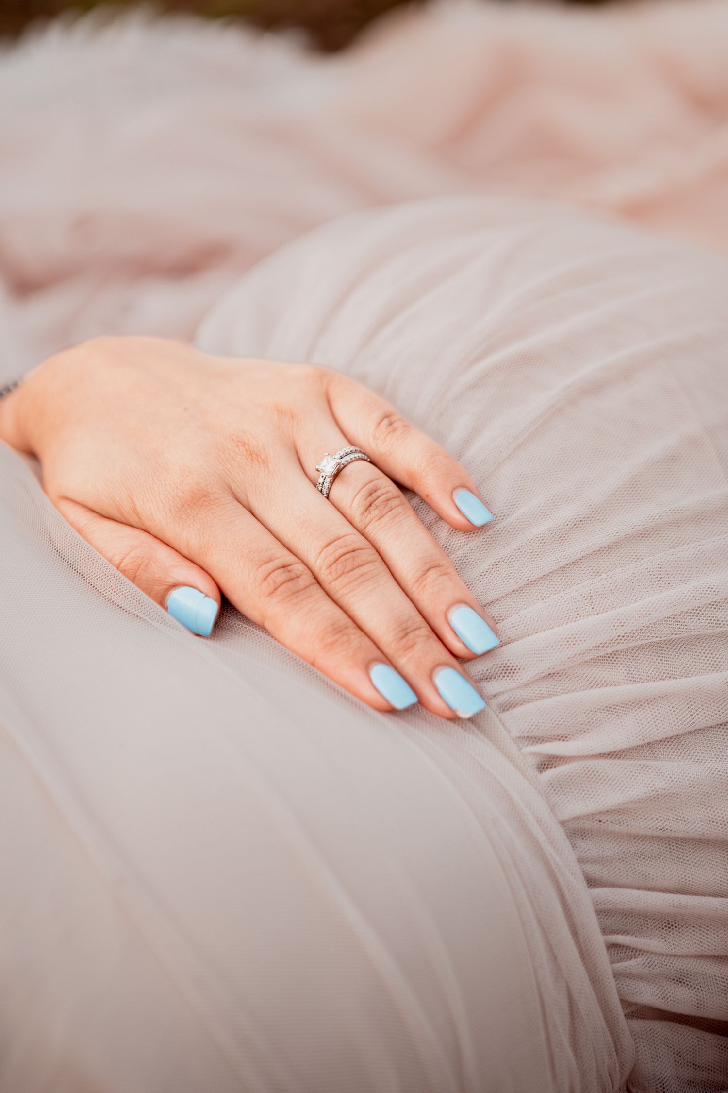 A hand with light blue nail polish rests delicately on soft pink tulle fabric.