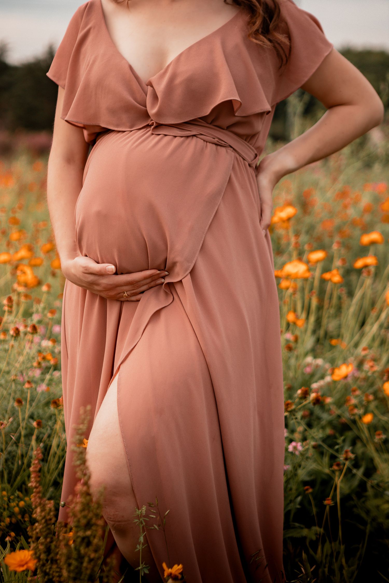 A flowy dusty rose maternity dress with ruffles photographed in a field of orange wildflowers.