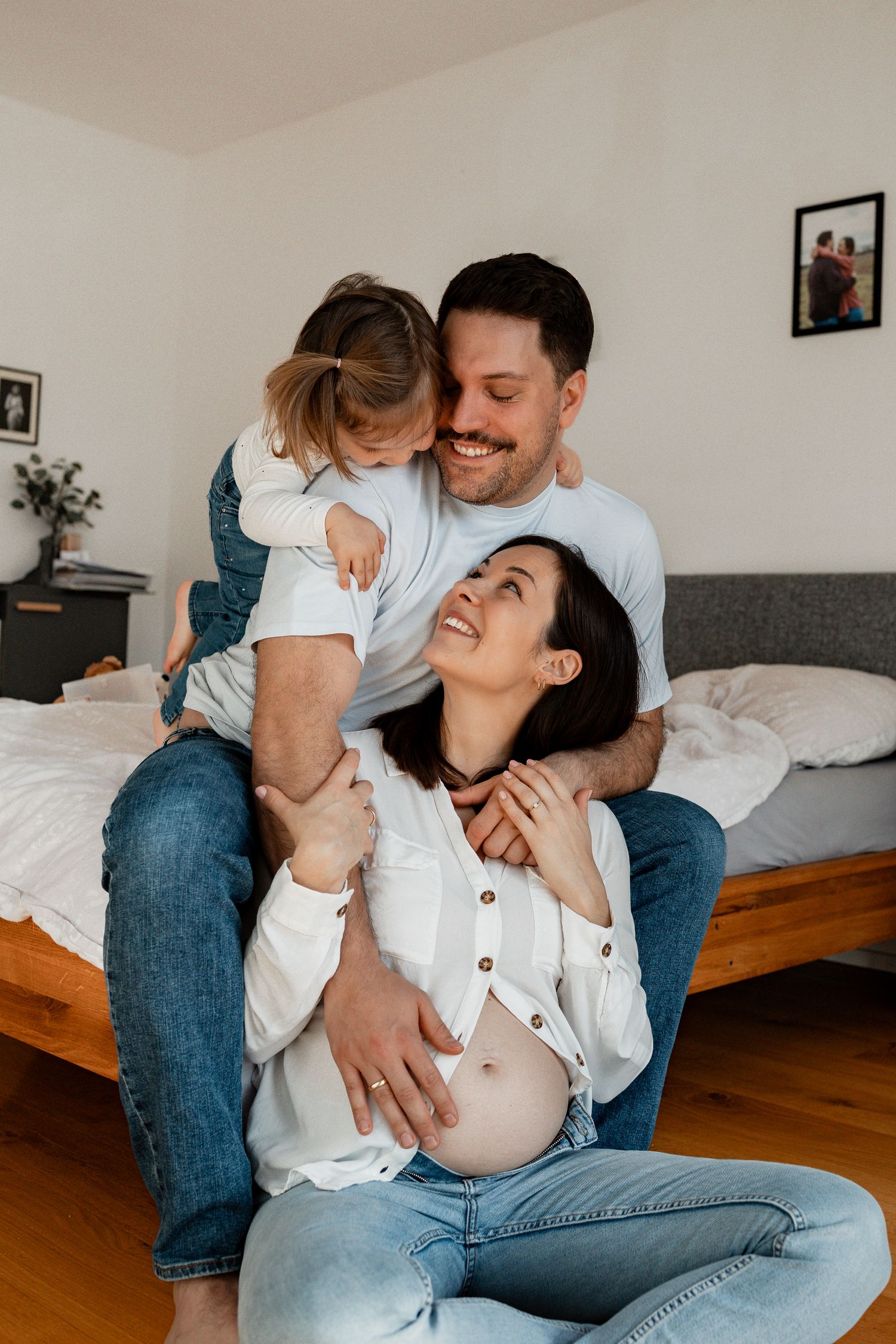 A couple shares intimate laughs and embraces while sitting together on a couch in a casual home setting.
