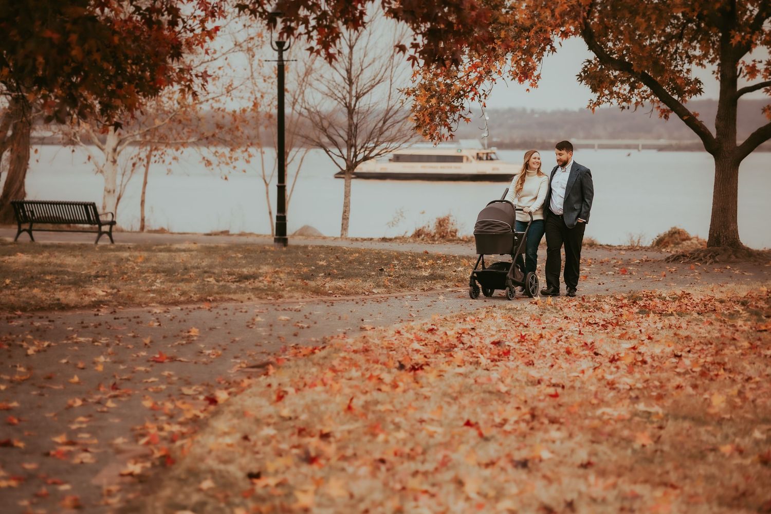 A romantic autumn photoshoot in a park with orange fallen leaves covering the ground and trees in the background.