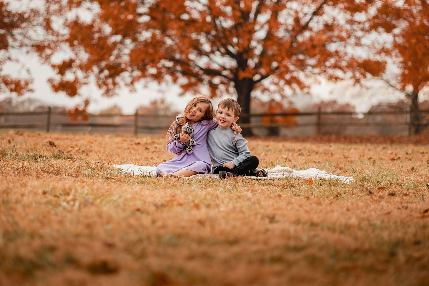 People relaxing on blanket under trees with vibrant orange fall foliage in park setting.