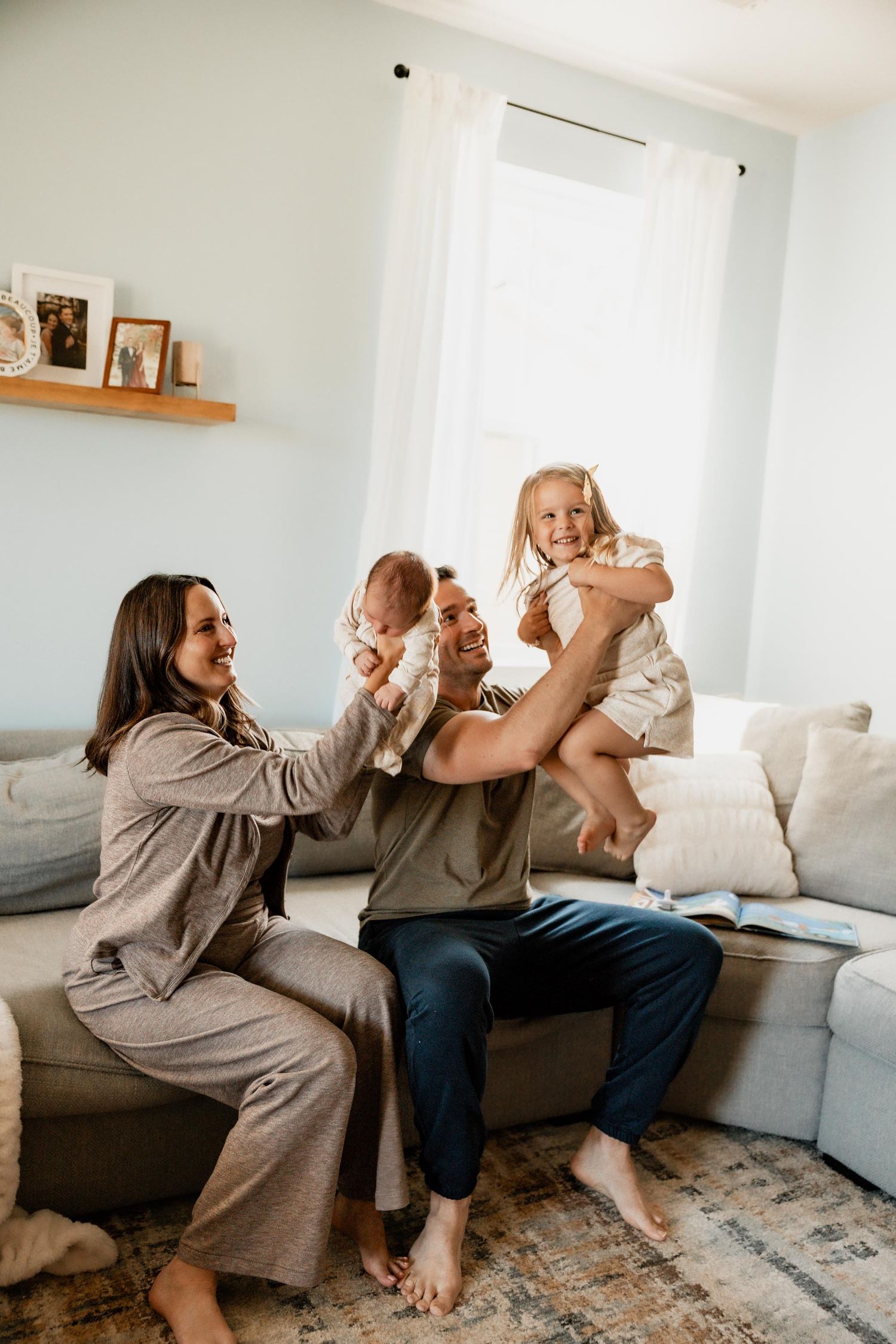 Happy family with two children playing on a couch in a bright living room.