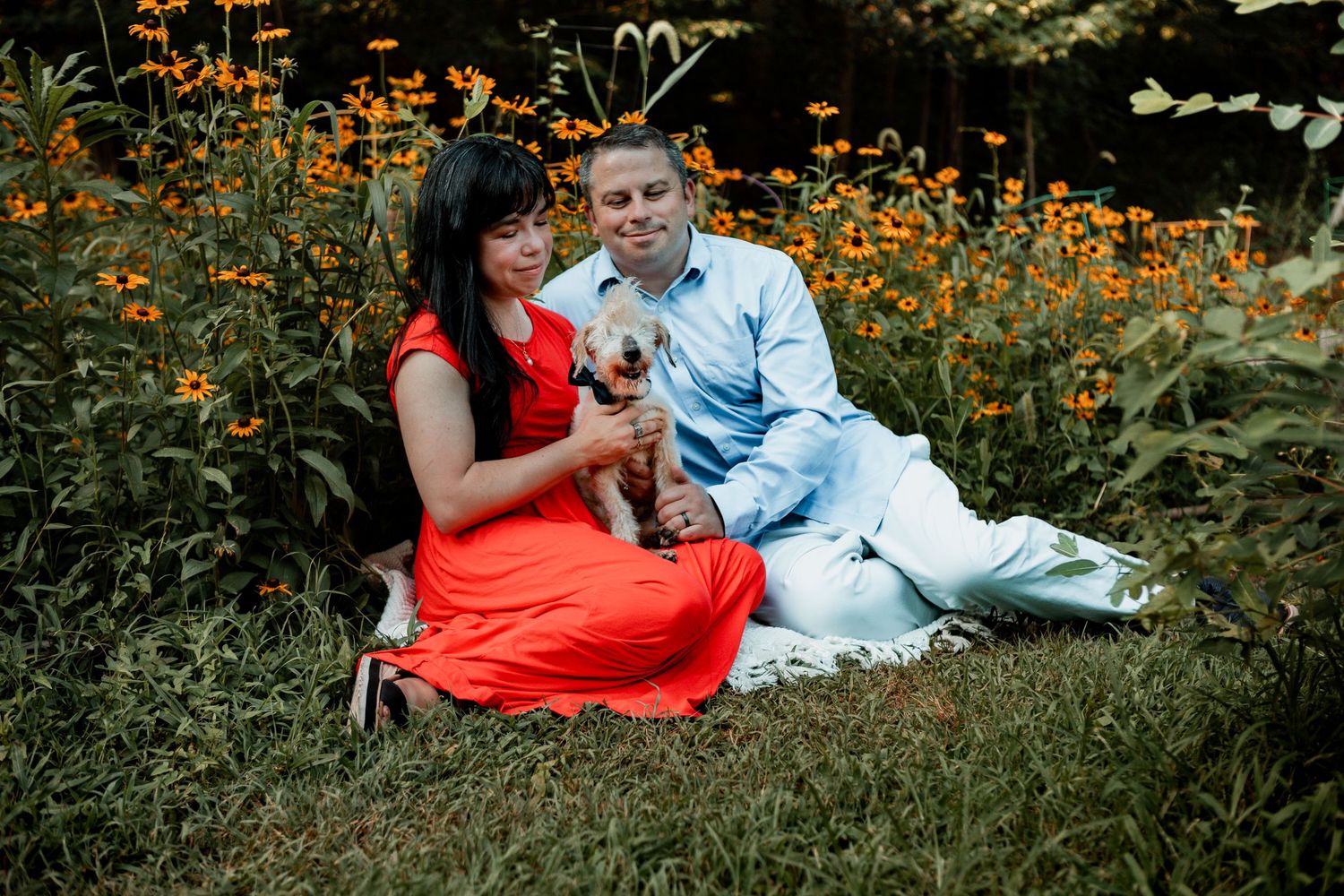 Couple sits together in a flowering garden with vibrant orange blooms surrounding them on a summer day.