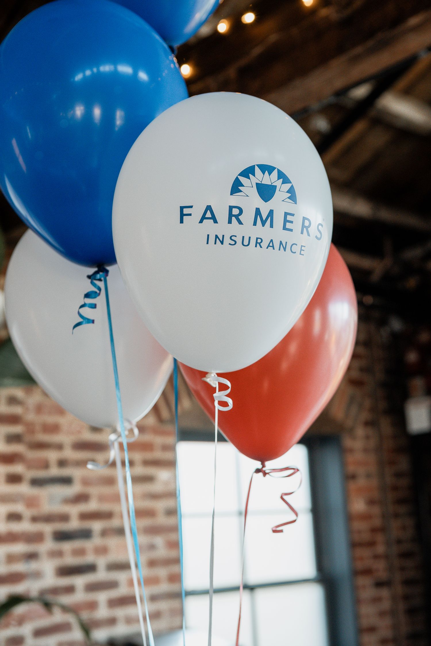 Farmers Insurance branded blue and white balloons arranged against a brick wall at an event.
