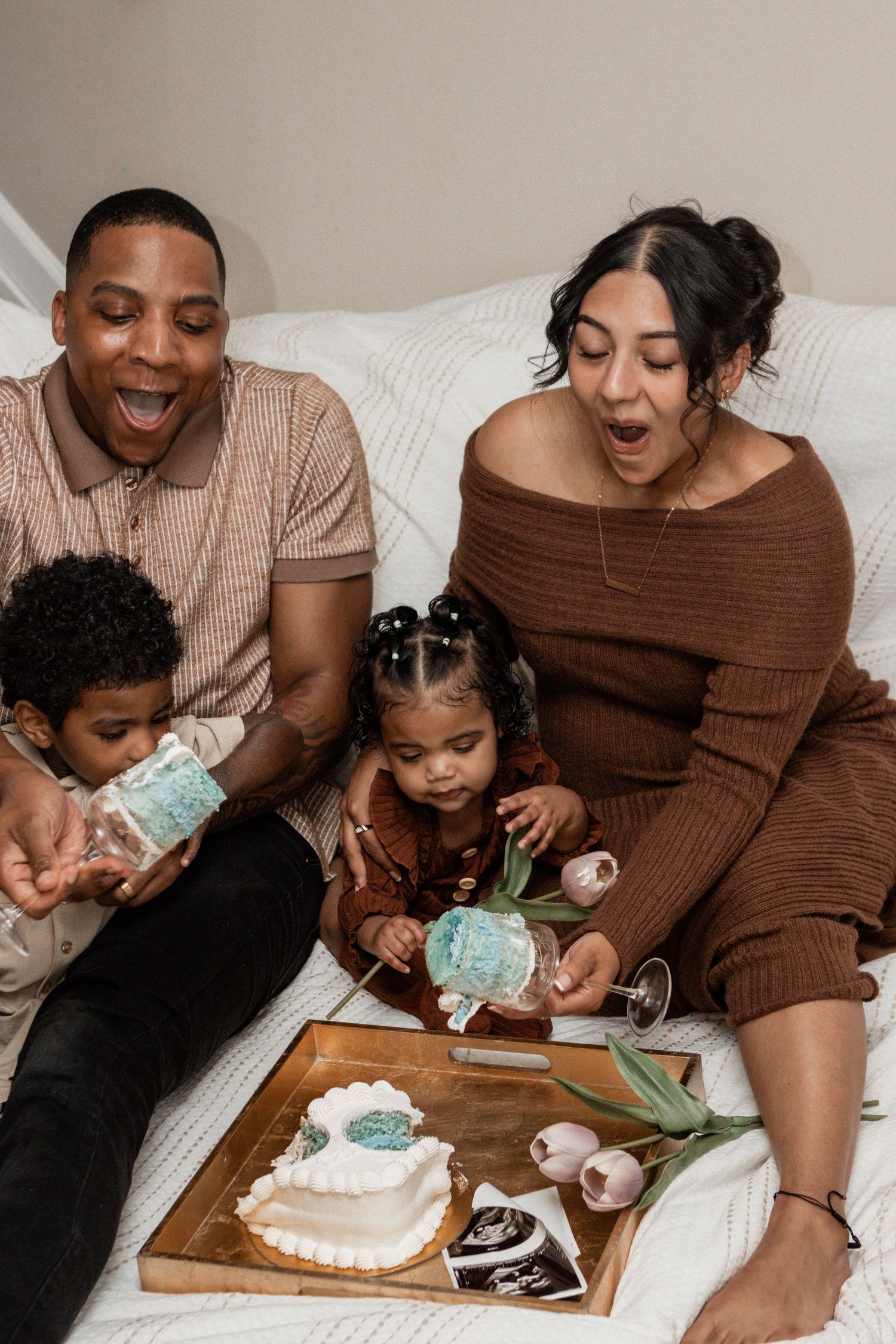 A family enjoys a cake decorating moment together while sitting on a white couch with dessert and decorating supplies.
