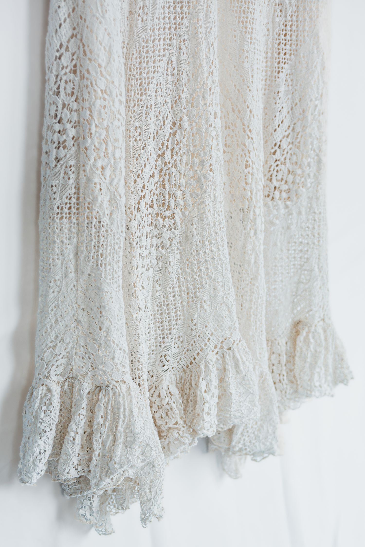 Close-up detail of white lace wedding dress fabric with delicate floral patterns and intricate embroidery.