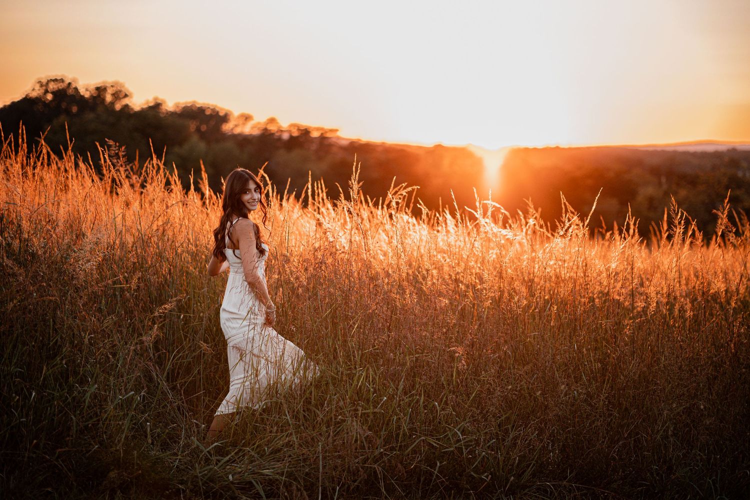 Silhouetted figures walk through tall grass against a glowing orange sunset backdrop in a dreamy rural setting.