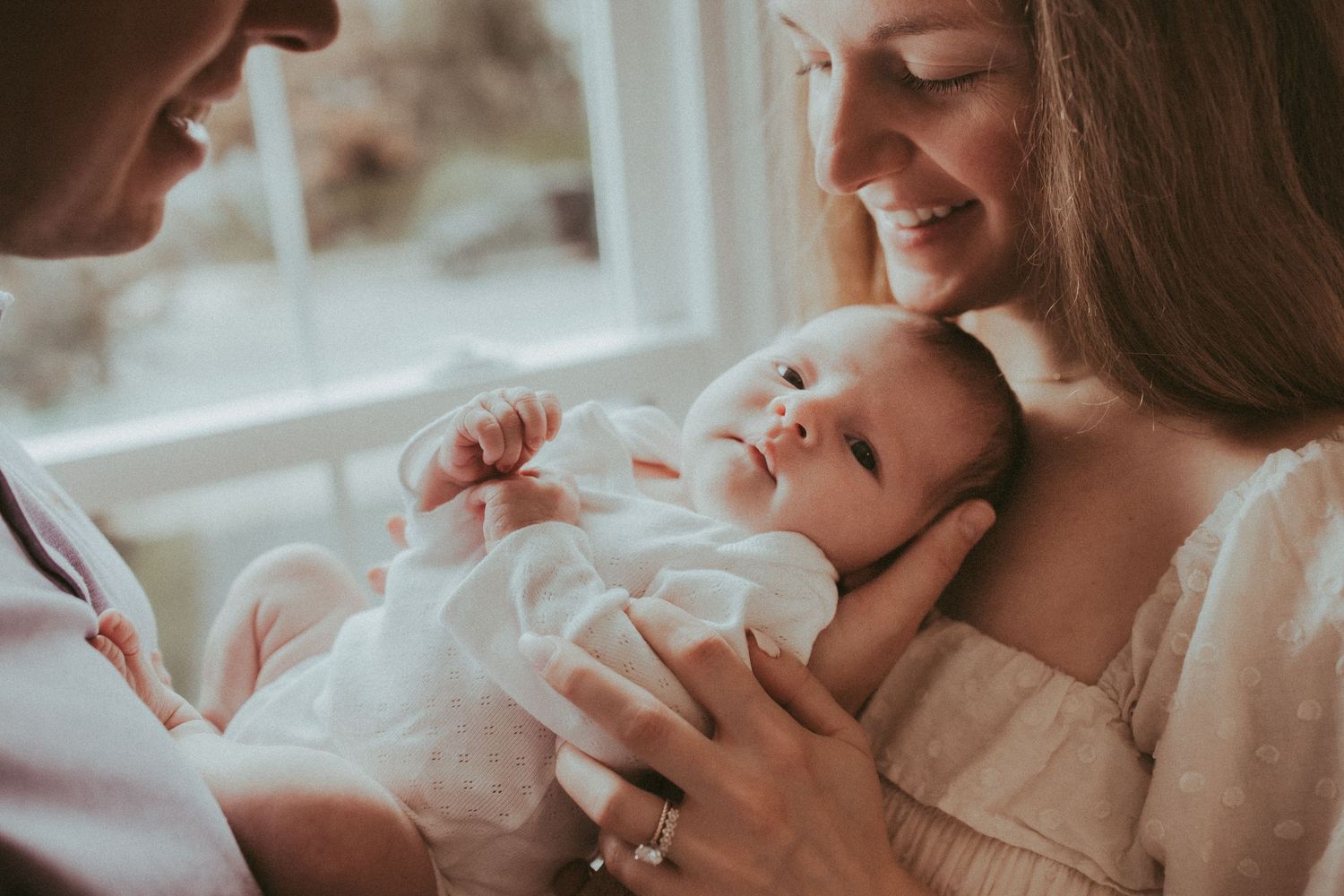 A tender moment between parent and newborn baby in soft natural lighting, showcasing gentle nurturing care.
