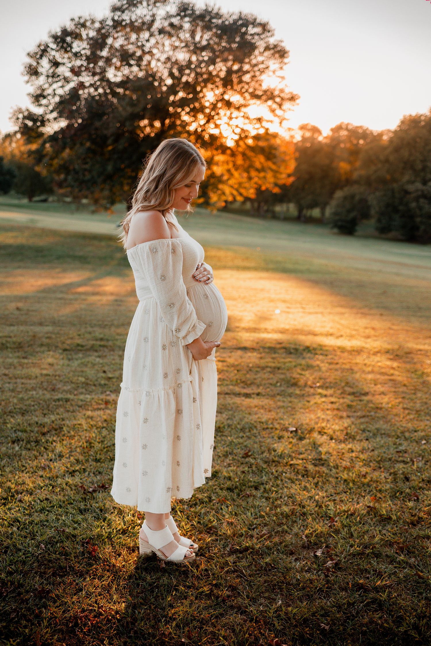 A figure in a flowing white dress stands in a golden sunlit field during sunset.